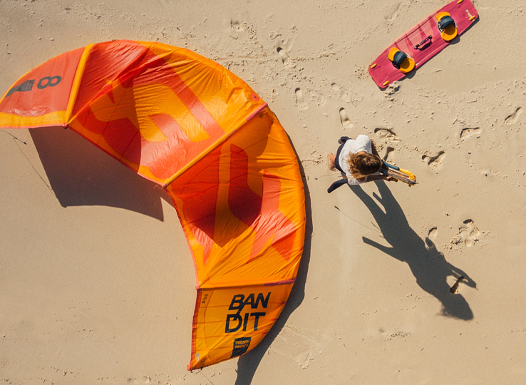 Kitesurf Lexikon: Orange Bandit kite on sandy beach with kitesurfer - kiteboarding equipment and water sports