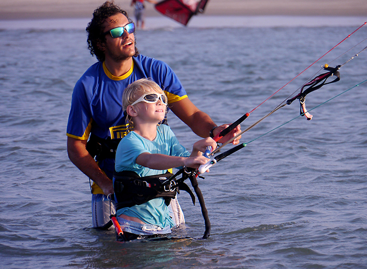Lezione di kitesurf con Kitesurfkurs - istruttore insegna kiteboarding a bambino in acqua, sport acquatici