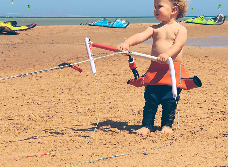 Bambino che impara kitesurf su spiaggia sabbiosa - lezioni kitesurf per bambini destinazione sport acquatici