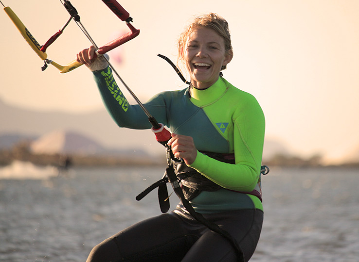 Kitesurfer sorridente in muta con barra kite in spiaggia - destinazione sport acquatici kiteboarding